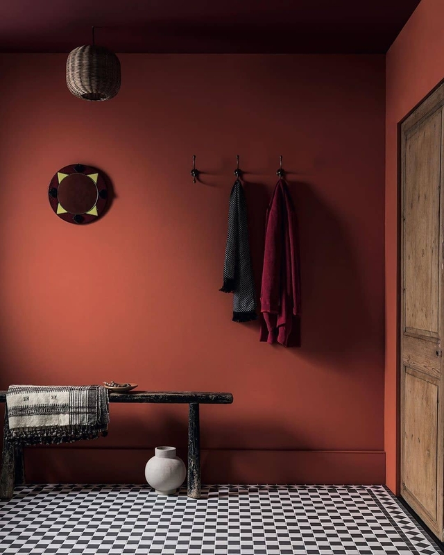 Hall de entrada em tom escuro com paredes na cor Vermelho Cereja Suvinil, um cabideiro e decorações em marrom.