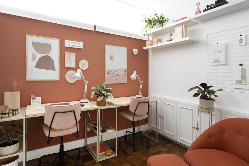 Home office com parede na cor Tamarindo Suvinil | Detalhes como quadros, plantas, mesa de madeira e cadeira rosa