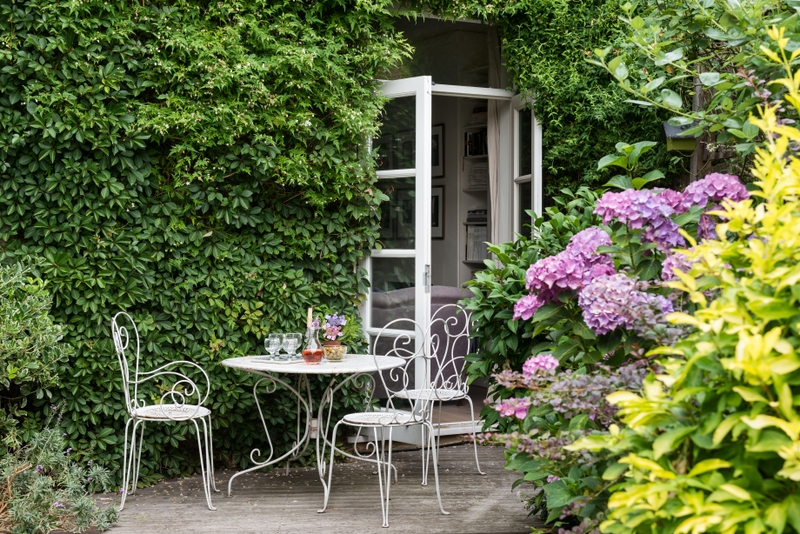 Jardim com tons de verde e flores roxas | Mesa e cadeiras de metal renovadas com Suvinil Esmalte Contra Ferrugem Jardim com tons de verde e flores roxas | Mesa e cadeiras de metal renovadas com Suvinil Esmalte Contra Ferrugem