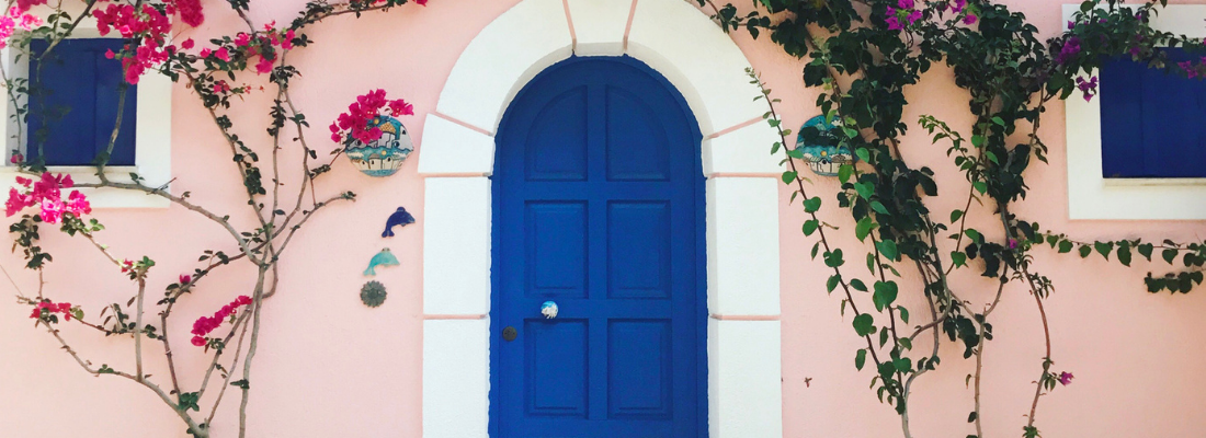 Fachada de casa com janelas e porta azul escuro, com bordas de cor branca e paredes rosa claro.
