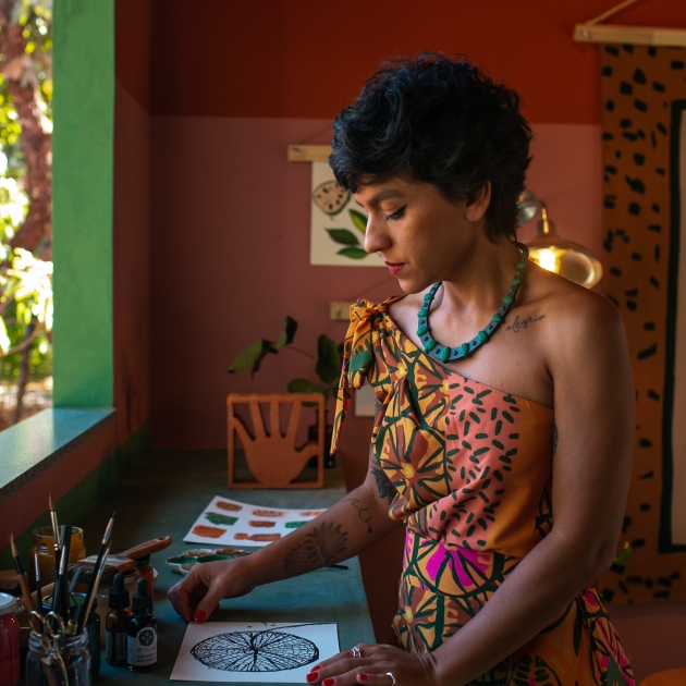 Mulher, observando uma desenho sobre uma bancada, em um ambiente com paleta de cores do Cerrado.